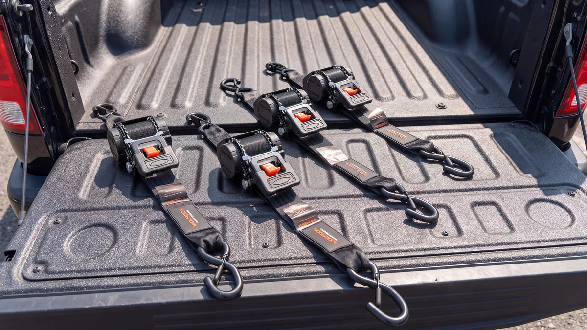 Retractable ratchet straps laid out flat and neatly stored in a pickup bed, keeping webbing wound inside the spool with no loose tails or tangles.