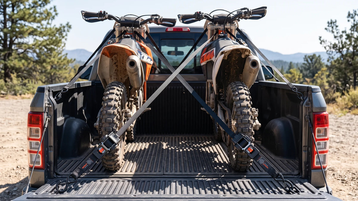 Two dirt bikes secured in a pickup bed with retractable ratchet straps, a ready setup for hauling powersports gear to the trail or the track.